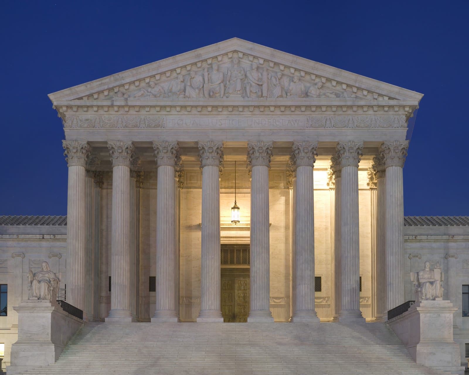 The west facade of the U.S. Supreme Court Building lit at dusk, with its columns and pediment against a deep blue sky